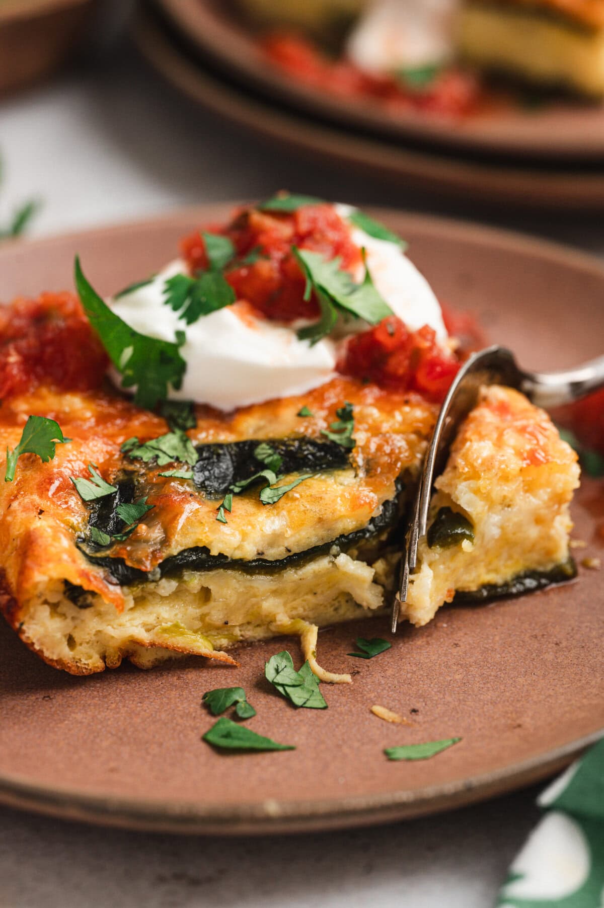 Piece of chile relleno casserole with salsa, sour cream, and cilantro on a plate.