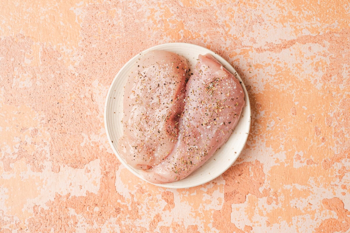 Raw chicken breasts with seasoning on a white plate