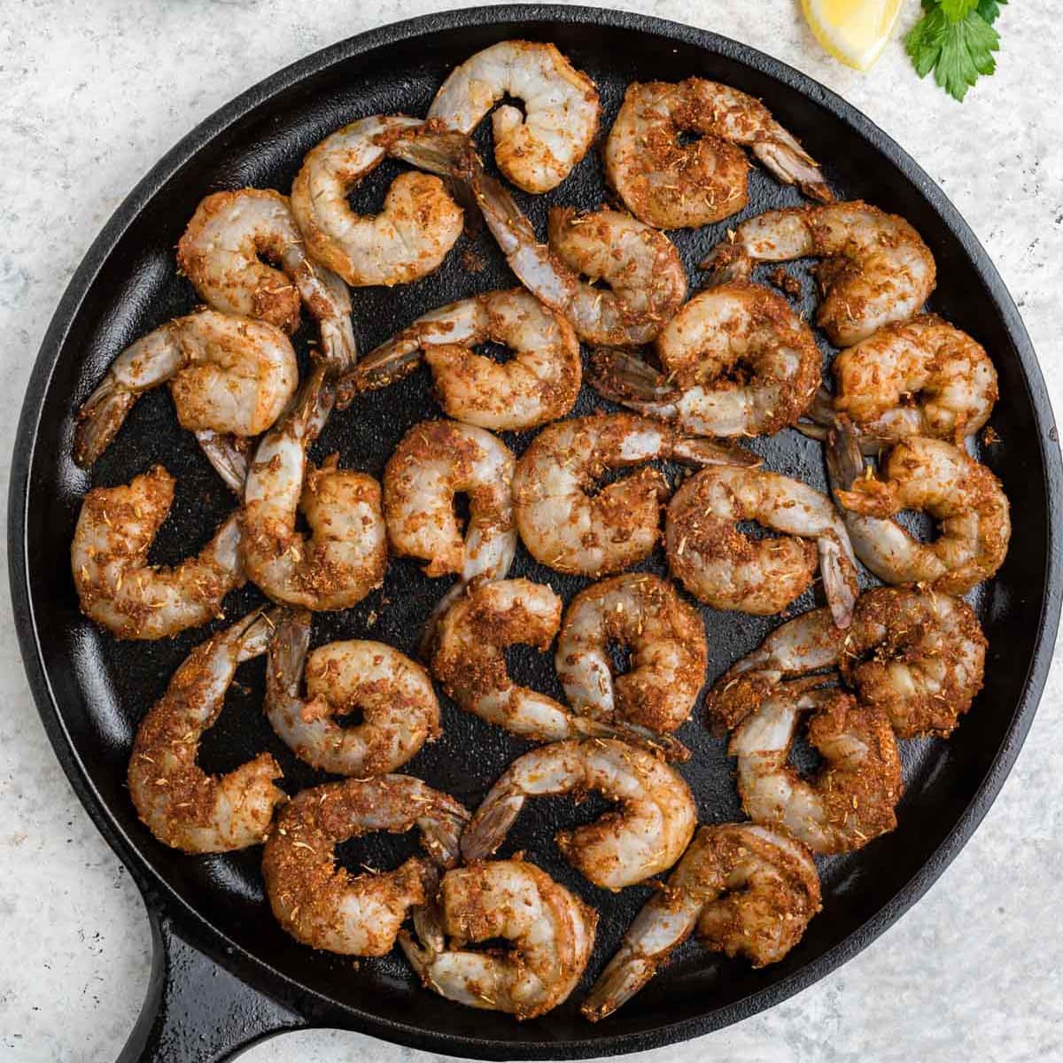 Blackened shrimp partially cooked in a cast iron pan.