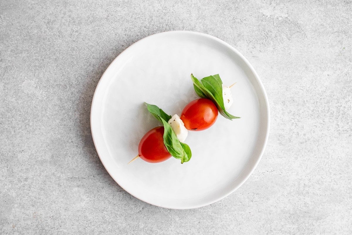 Tomato, basil, and mozzarella on skewer on a white plate