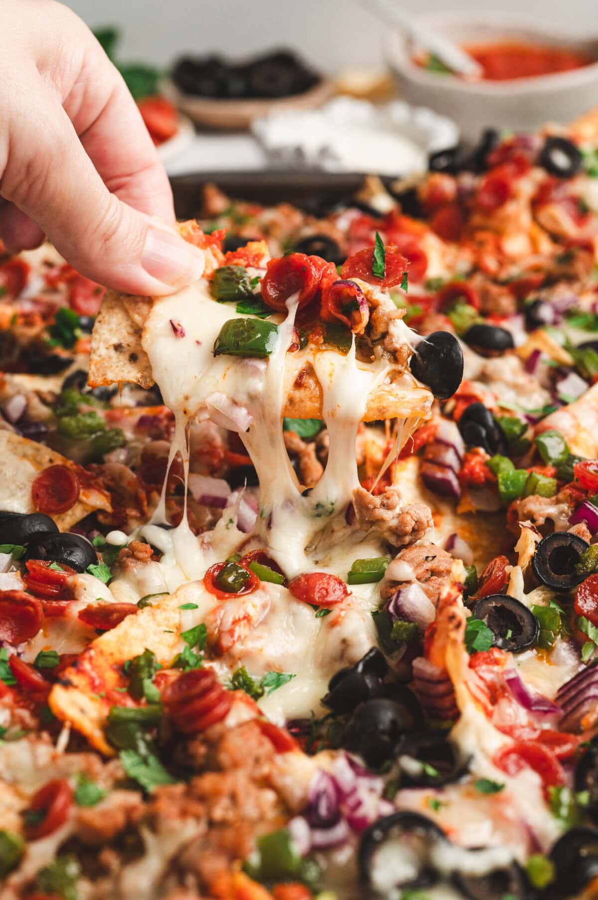Close up of hand holding up a piece of loaded pizza nachos