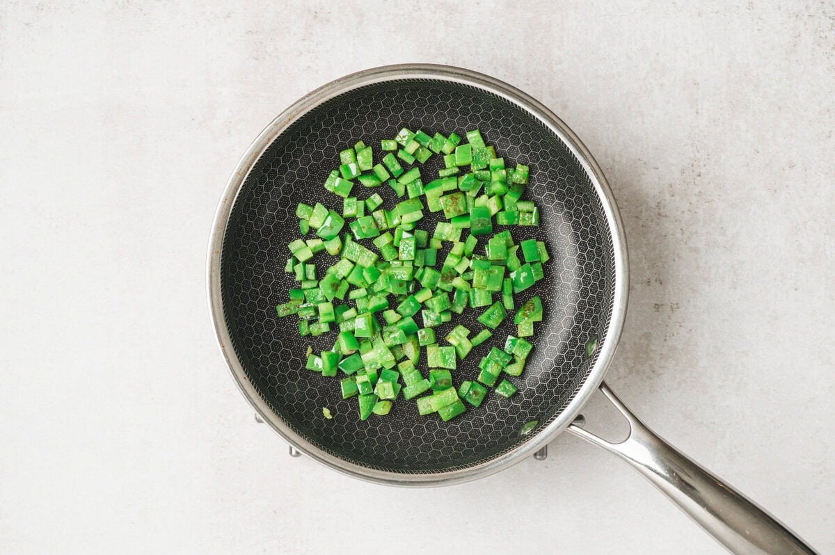 Diced green bell pepper being sauteed in a sauté pan.