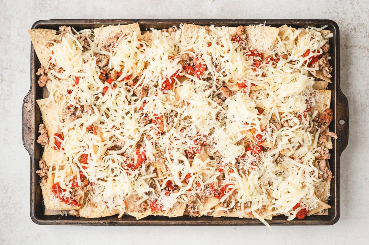 Unbaked chips on a sheet pan with sausage, pizza sauce, and shredded cheese.