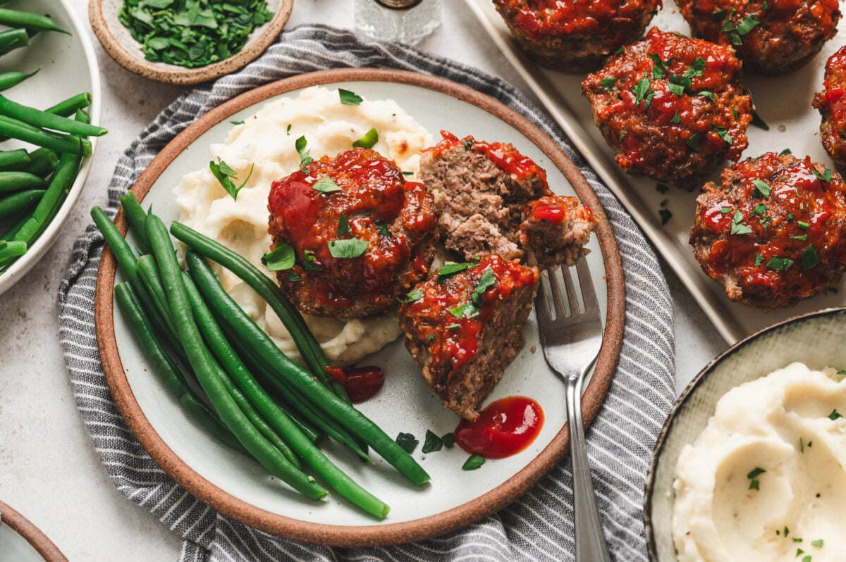 Mini meatloaves with ketchup glaze on a plate with mashed potatoes and green beans.