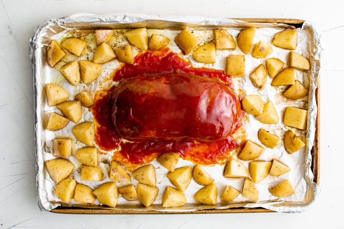 Glazed meatloaf on a sheet pan with diced unbaked potatoes.