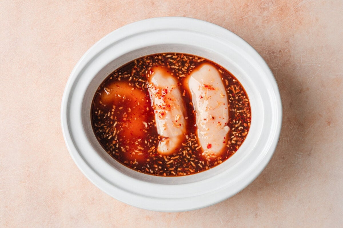 Raw chicken in white slow cooker insert with honey garlic sauce