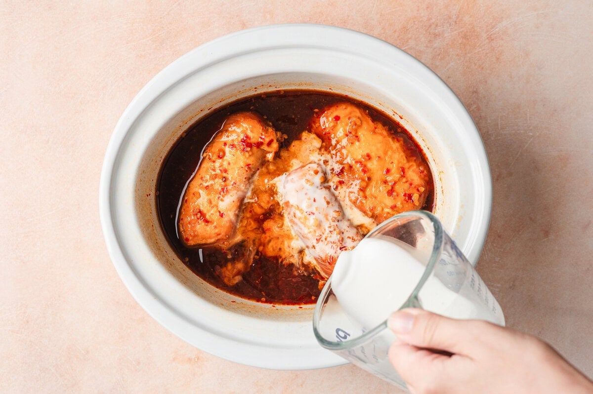 Cooked honey garlic chicken with cornstarch slurry being poured in