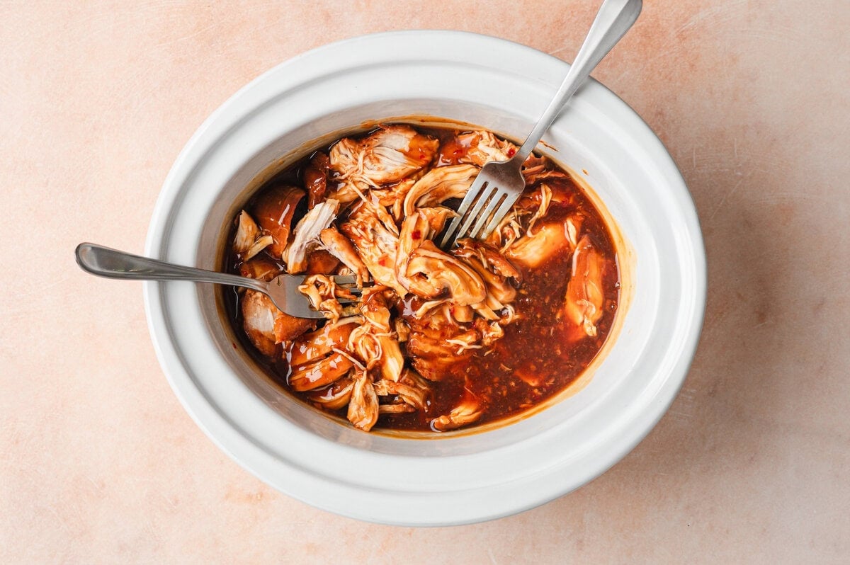 Shredded cooked honey garlic chicken in white slow cooker insert.